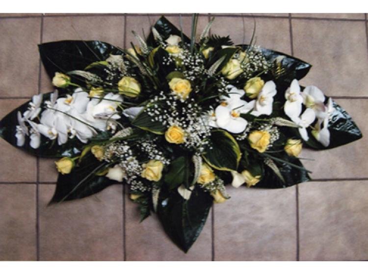 Langwerpig bloemstuk met donkergroene bladen witte orchideeën en gele rozen
